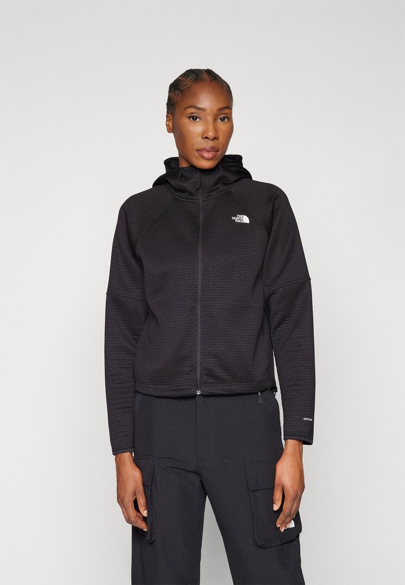 Crna zip-up hoodie s teksturiranim dizajnom, visokim ovratnikom i logom na prsima. Uparen s odgovarajućim cargo hlačama.