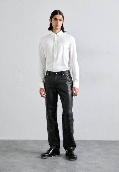 Biela košeľa s dlhými rukávmi a vreckom, skombinovaná so štruktúrovanými čiernymi nohavicami s diamantom. Čierne topánky dotvárajú outfit.