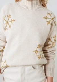 Beige Rollkragenpullover mit geripptem Kragen. Goldene Schneeflockenmuster an den Ärmeln. Weiche Stricktextur, lockere Passform.