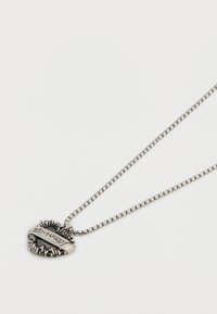 Ασημένιο μενταγιόν σε σχήμα καρδιάς με περίγραμμα από στριφογυριστό σχοινί, χαραγμένο με τη λέξη "Ed Hardy", κρεμασμένο από ασημένια αλυσίδα πάνω σε λευκό φόντο.