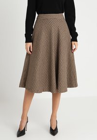 Ruskeanruudullinen midihame, joka on valmistettu teksturoidusta kankaasta, istuvalla vyötäröllä ja liehuleikkauksella, yhdistetty mustiin korkokenkiin.