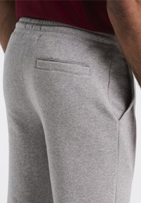 Graue Jogginghose aus weichem Stoff, mit einer Seitentasche und einem elastischen Bund für zusätzlichen Komfort. Einfaches Design ohne sichtbare Muster.