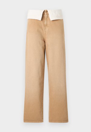 Pantalon large à taille haute beige avec fermeture visible par bouton et fermeture éclair, assorti d'un col de chemise blanc rentré.