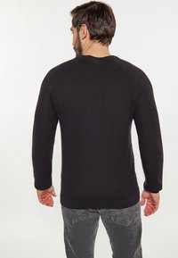 Zwarte, gestructureerde trui met lange raglanmouwen, ronde halslijn en geribbelde zoom. Draag met donkergrijze jeans, gezien vanaf de achterkant.