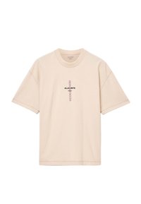 Camiseta de algodón beige con mangas cortas, cuello redondo y detalle de logo en el frente. Presenta un corte relajado y costuras visibles.