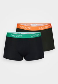 Two pairs of boxers, one navy with a green waistband, the other dark green with an orange waistband, featuring the Lacoste logo on each.