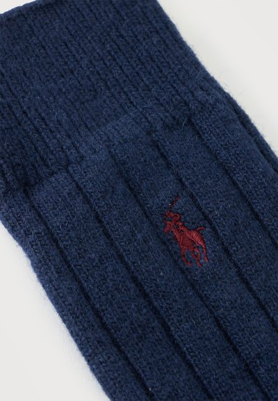 Tissu en maille côtelée bleu foncé avec un petit logo brodé rouge de joueur de polo centré sur le matériau.