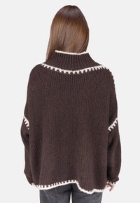 Brauner Strickpullover mit hohem Kragen, weißem geometrischem Muster entlang der Schultern und Ärmel, lockere Passform mit strukturierter Oberfläche.