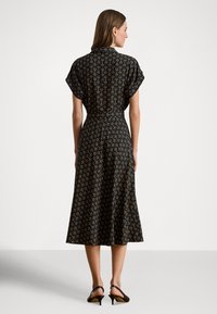 Vestido preto de manga curta, com padrão de linhas amarelas. Comprimento midi evasê com cintura ajustada, combinado com sandálias pretas de salto.