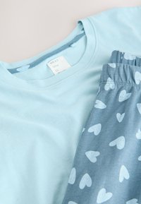 T-shirt en coton bleu clair avec un col rond, accompagné d'un pantalon de pyjama gris orné d'un motif de cœurs blancs et d'une taille élastique.