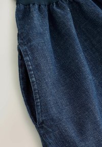 Tissu en denim bleu foncé avec une ceinture élastique et une poche latérale visible à gauche.