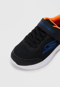 Schwarzer Sportschuh aus Mesh mit orangefarbenen Akzenten. Verfügt über einen Riemen und Schnürsenkel, mit einer weißen Sohle und blauen Logodetails.