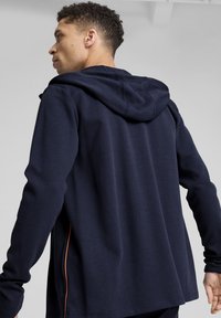 Felpa navy con cappuccio, realizzata in un morbido tessuto testurizzato, dotata di cappuccio regolabile e dettagli laterali arancioni a contrasto; vestibilità rilassata con maniche lunghe.