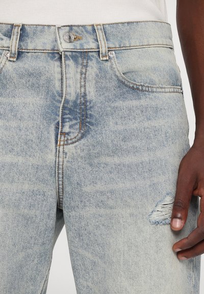 Lyseblå denim jeans med en falmet finish, der har fem lommer og en slidt detalje på højre lår. Metalknaplukning.