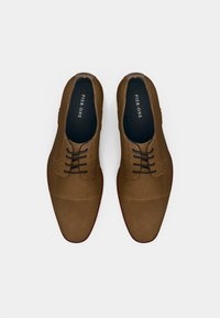 Par de sapatos de vestir em couro castanho texturizado com atacadores pretos, solas vermelhas e palmilhas "PIER ONE" sobre um fundo branco.