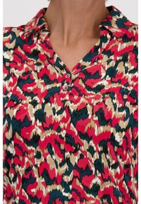 Multikleurenblouse met een levendig abstract patroon in rood, groen en bruin. Inclusief een kraag en knoopdetails aan de voorkant.