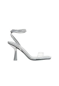 Transparante sandalen met een doorzichtig bovenwerk, versierd met zilveren studs en een delicaat enkelbandje, geplaatst op een slanke hak.