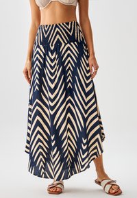 Falda larga azul marino y crema con patrones de chevron, cintura fruncida y tela fluida. Combinada con sandalias planas.