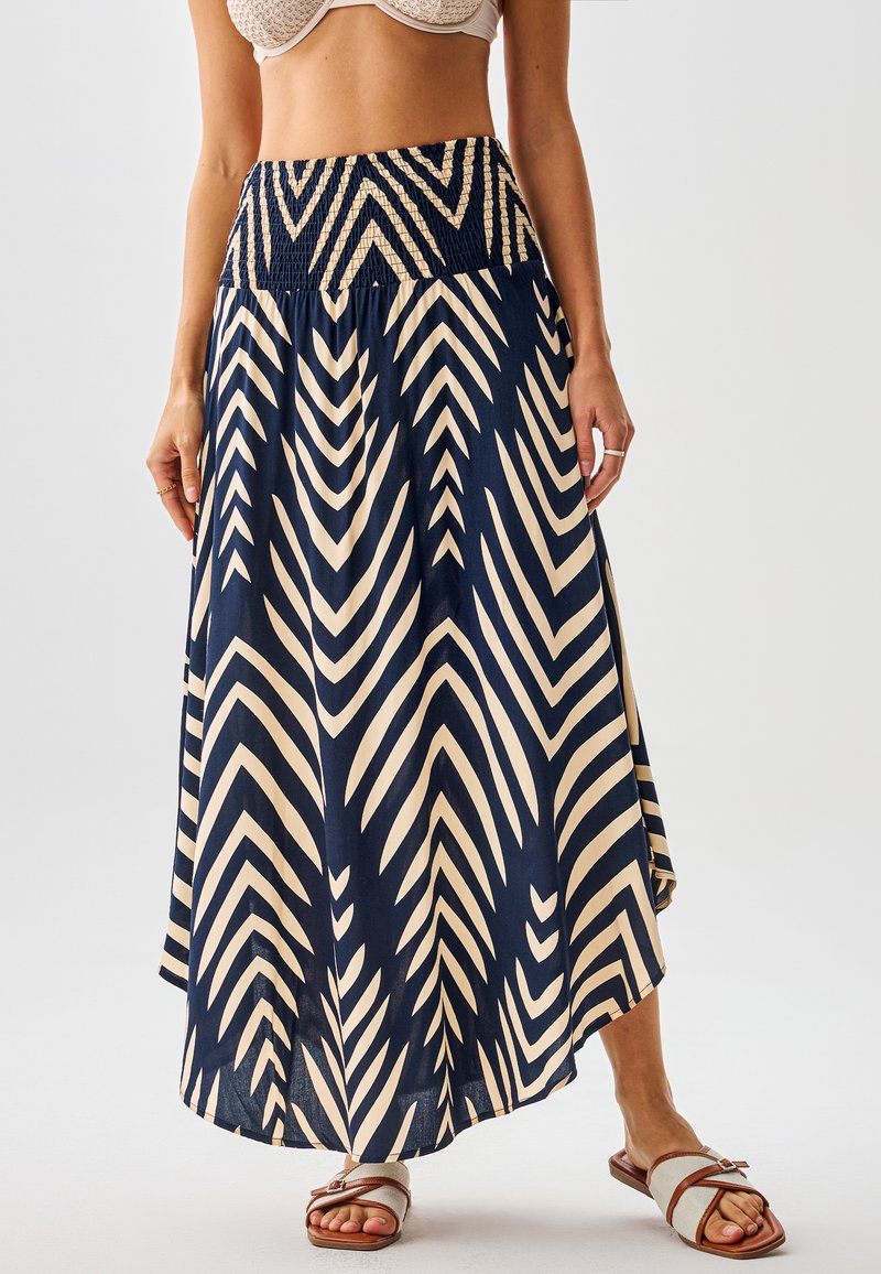 Falda larga azul marino y crema con patrones de chevron, cintura fruncida y tela fluida. Combinada con sandalias planas.