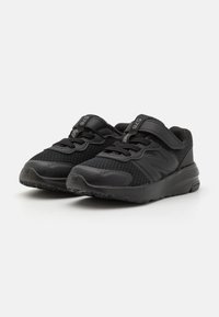 Baskets de sport noires avec une tige en mesh et en synthétique, dotées d'une sangle Velcro, de lacets et d'une semelle en caoutchouc texturé pour une adhérence et une durabilité.