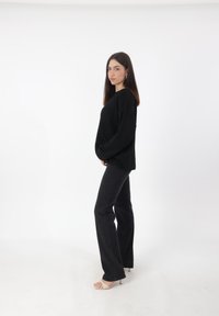 Zwarte oversized trui met een gestructureerde afwerking, gecombineerd met zwarte flared jeans en lichtgekleurde hakkensandalen. Eenvoudig, minimalistisch ontwerp.
