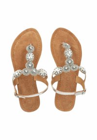 Sandali piatti con una suola in suede color tan. Strappi decorativi argentati con gemme finte circolari e cinturino alla caviglia regolabile.