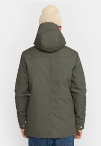 Olivgrüne Kapuzenjacke mit glatter Textur, geradem Schnitt und Knopfverschlüssen an den Bündchen. Trägt eine hellbeige gestrickte Mütze.