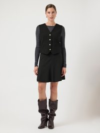 Musta liivi, jossa viisi hopeanväristä nappia, pidetty mustan mekon päällä. Polven korkeudelle ulottuvat ruskeat nahkasaappaat, joissa rennon rypytetty muotoilu ja sileä pinta.