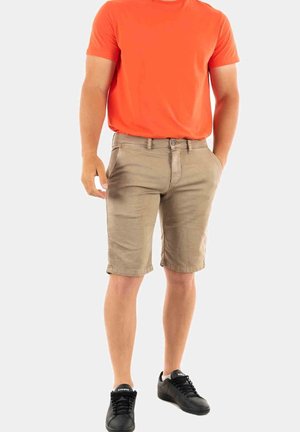 Conjunto masculino que presenta una camiseta de manga corta naranja brillante, pantalones cortos beige hasta la rodilla y zapatillas negras. Diseño simple con bolsillos.
