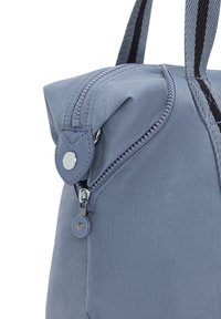 Lys blå nylon taske med et struktureret design, der har en lynlås i toppen, læderdetaljer og dobbelte håndtag med sort og grå striber.