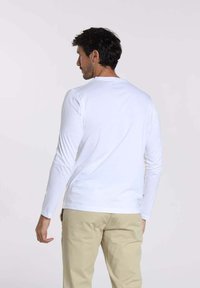 T-shirt à manches longues blanc en tissu doux, doté d'un col rond et d'un design ajusté, associé à un pantalon beige clair.