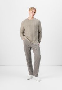 Pull en maille beige associé à un pantalon en velours côtelé gris clair et des baskets blanches ; coupe décontractée, manches longues et poches latérales sur le pantalon.