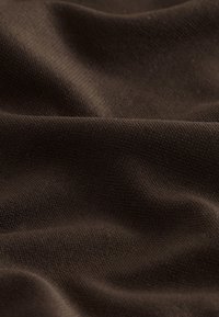 Tissu doux brun foncé avec une surface lisse, légèrement texturée, et des plis délicats créant des ombres et de la profondeur.