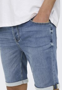 Lichtblauwe denim shorts met een opgerolde zoom. Kent een klassiek vijf-pocket ontwerp en subtiele vervaging. Materiaal lijkt zacht en gestructureerd.