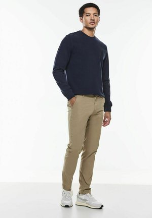 Navy sweatshirt with crew neck, paired with beige chinos. Model wearing white sneakers. Smooth fabric with a relaxed fit. Minimalist design.
