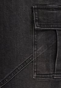 črn denim material z teksturirano površino, z obližno žepom in diagonalnimi šivi, ki poudarjajo trpežen, estructuriran dizajn.