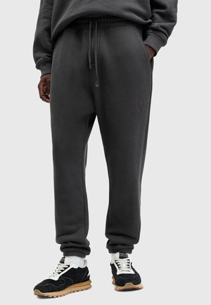 Pantalons de jogging gris foncé avec une taille élastique, des poches latérales et des poignets côtelés. Présente un logo brodé discret à l'avant.