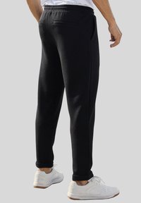 Schwarze Sweatpants aus weichem Stoff, mit schlankem Schnitt, seitlichen Taschen und einem umschlagenen Saum, kombiniert mit weißen Turnschuhen.