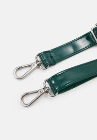 Zelený patentovaný kožený pásek se st říbrnými kovovými sponami. Vyznačuje se lesklou texturou a zesíleným prošíváním podél okrajů.