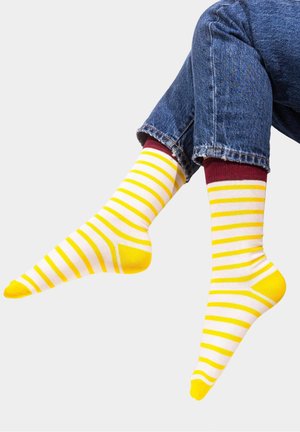 Żółto-białe skarpetki w pasy z bordowym mankietem i żółtymi akcentami, wykonane z miękkiego materiału, pokazane noszone z dżinsami.