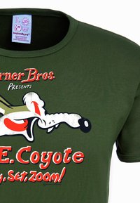 Camiseta de algodón verde oliva con un gráfico de Wile E. Coyote y un texto en rojo y blanco que dice: "¡Listo, listo, a toda velocidad!" en la parte delantera.