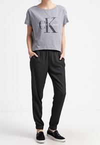 Szara krótka koszulka z logo "Calvin Klein Jeans", zestawiona z czarnymi dresami i czarnymi butami wsuwanymi. Codzienny, luźny fason.