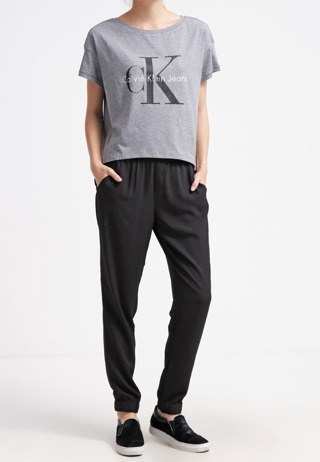 Szara krótka koszulka z logo "Calvin Klein Jeans", zestawiona z czarnymi dresami i czarnymi butami wsuwanymi. Codzienny, luźny fason.
