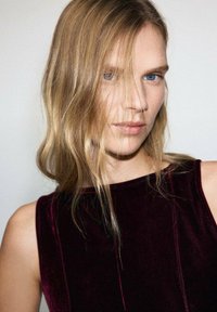 Rochie din catifea bordeaux cu un guler înalt și bretele laterale, având o textură netedă și linii verticale subtile pe un fundal neutru.