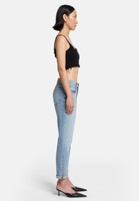Top corto nero e jeans high-waisted azzurri chiari, slim fit con risvolti, abbinati a décolleté nere a punta.