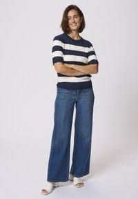 Un pull à rayures bleu marine et blanches à manches courtes associé à un jean bleu à jambes larges et des sandales à talons ouverts blanches. Tissu lisse et coupe décontractée.