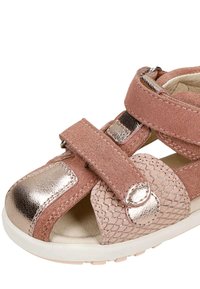Sandale rose pour enfants avec accents métalliques, brides réglables en velcro et panneau latéral texturé sur une semelle blanche.