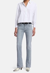 Witte blouse met knopen, lichtblauwe jeans met rechte pijpen, zwarte riem en witte enkellaarsjes met slangenprint en hak. Simpel en nauwsluitend model.