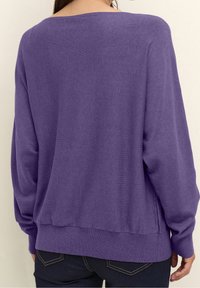 Lila stickad tröja med lös passform, bred halsringning och ribbat fåll. Har långa ärmar och en mjuk textur. Bakvy visas.