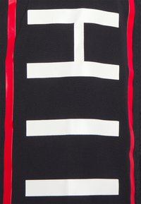 Tessuto nero con un audace grafico bianco che presenta elementi orizzontali e verticali, accentuato da una striscia verticale rossa sulla destra.